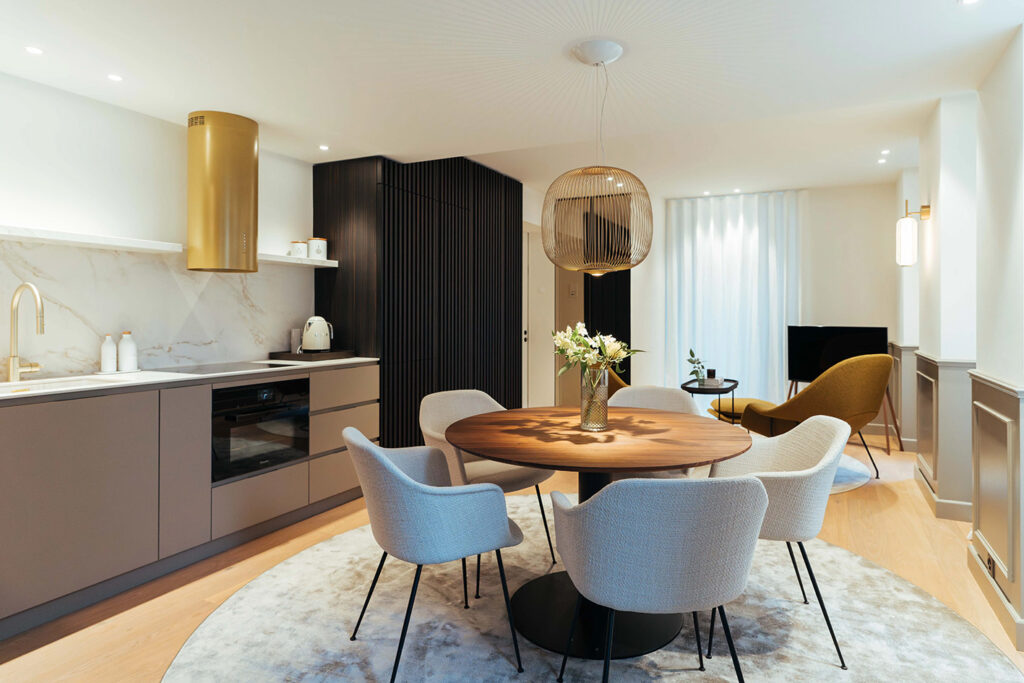 Moderne Küche mit goldiger Armatur und Dampfabzug sowie marmorähnlicher Abdeckung und stylischer Essbereich mit Holztisch, Polsterstühlen und goldener Hängelampe