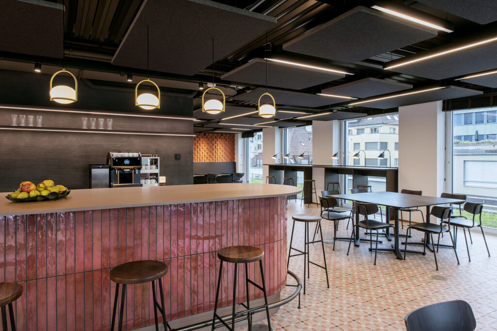 Moderne Cafeteria mit Bartheke und weiteren Tischen und Stühlen als Teil einer innovativen Arbeitswelt – hochwertiger Innenausbau umgesetzt von der Schreinerei R. Brunner AG Zürich