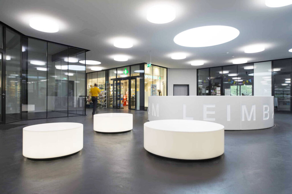 Eingangsbereich mit leuchtenden Sitzinseln und gebogener Empfangstheke im Einkaufszentrum Leimbach