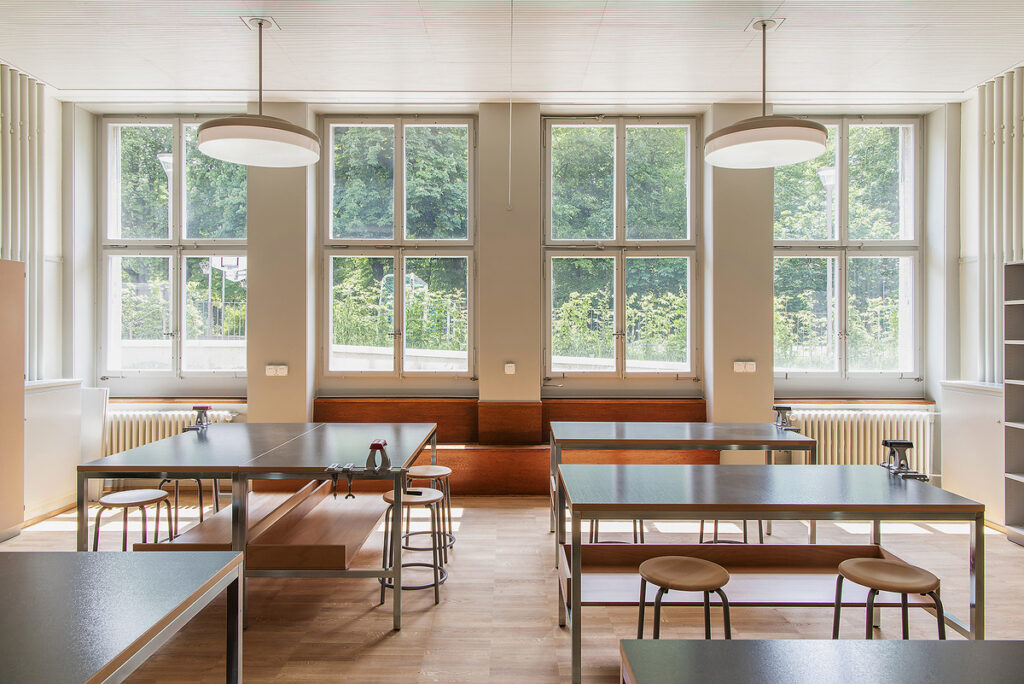 Werkraum mit Holzbänken, Hockern und grossen Fenstern im Schulhaus Gubel