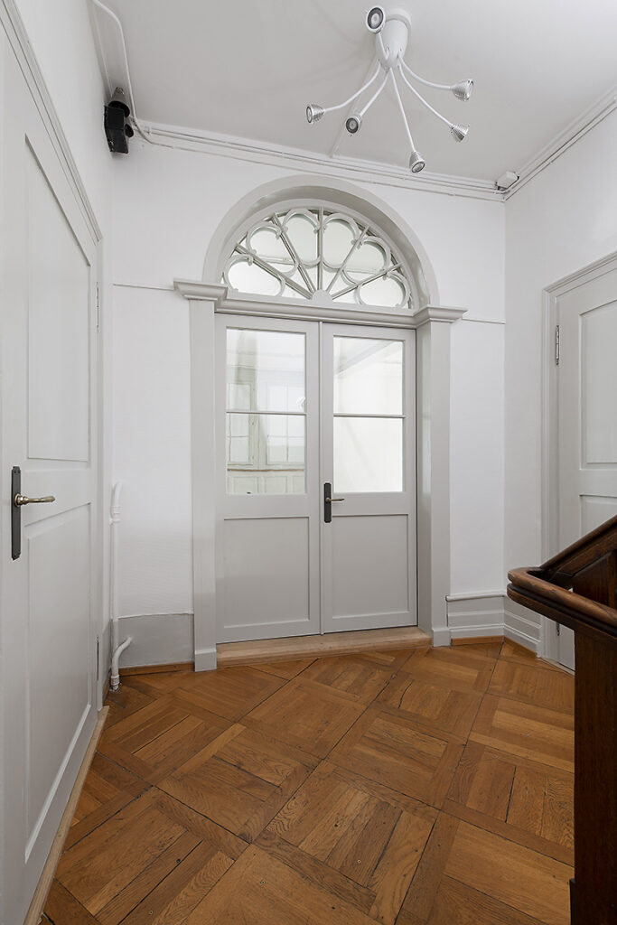 Doppelflügelige Holztüre mit halbkreisförmigem Oblicht und Glasfüllungen, Blick aus dem Treppenhaus