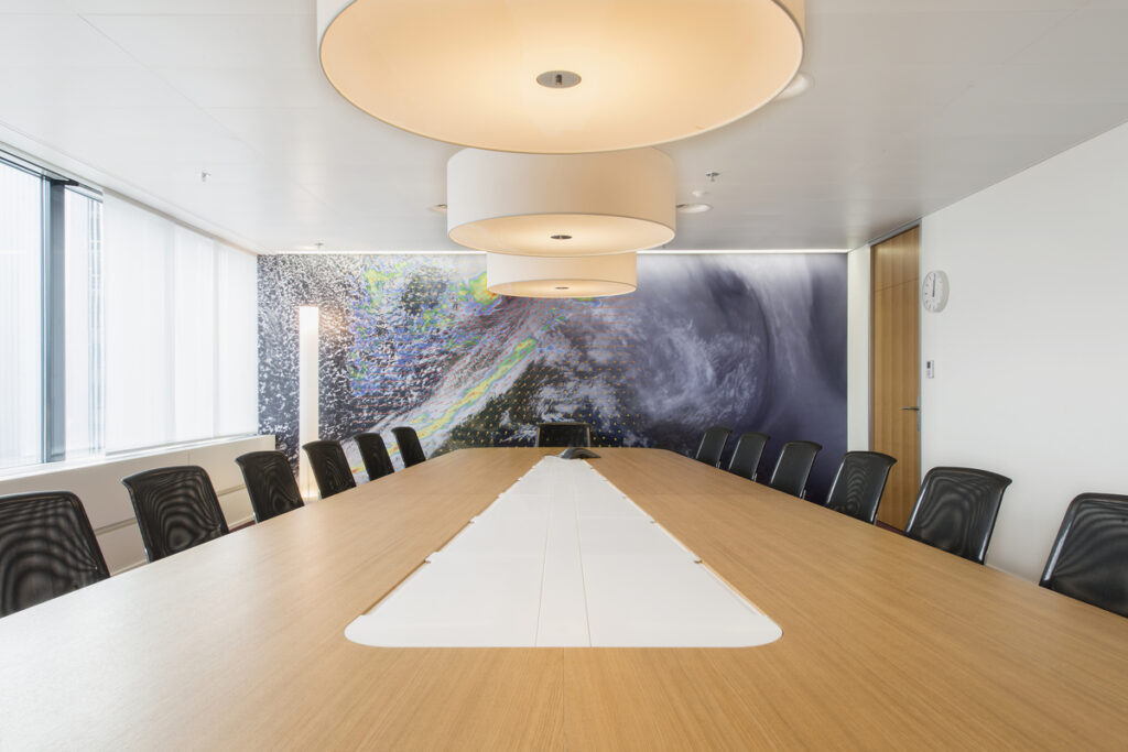 Grosser Meetingraum mit langem Holztisch, integrierter Techniklösung und Wandbild einer Wetteraufnahme.