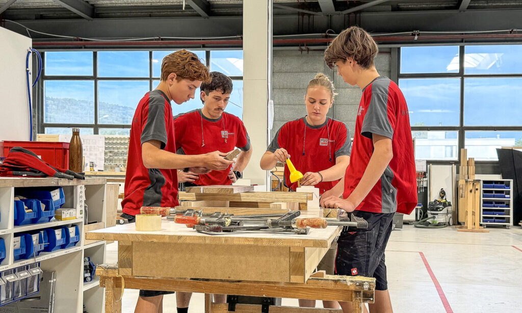 Drei Schreinerlernende arbeiten gemeinsam mit ihrem Berufsbildner an einem Werkstück aus Holz