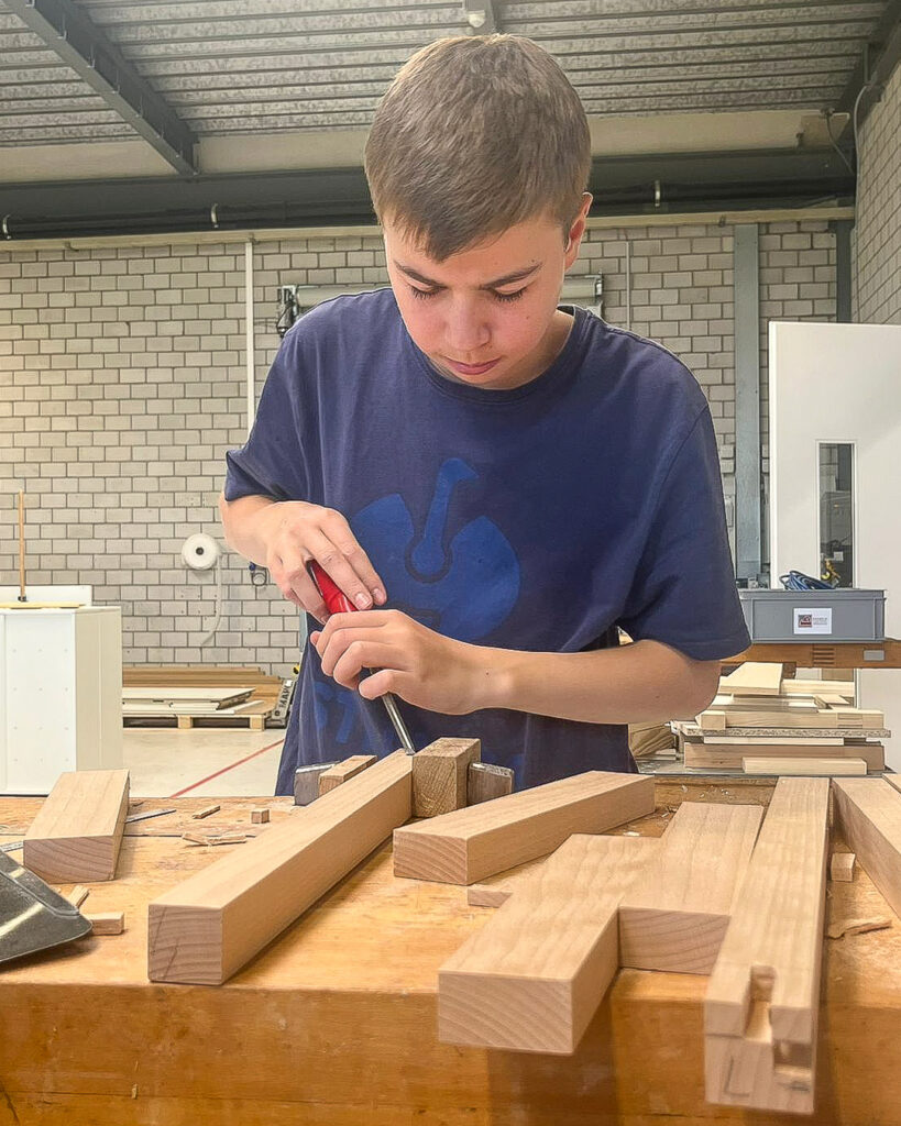 Schnupperlernender bearbeitet ein Holzstück mit einem Stechbeitel