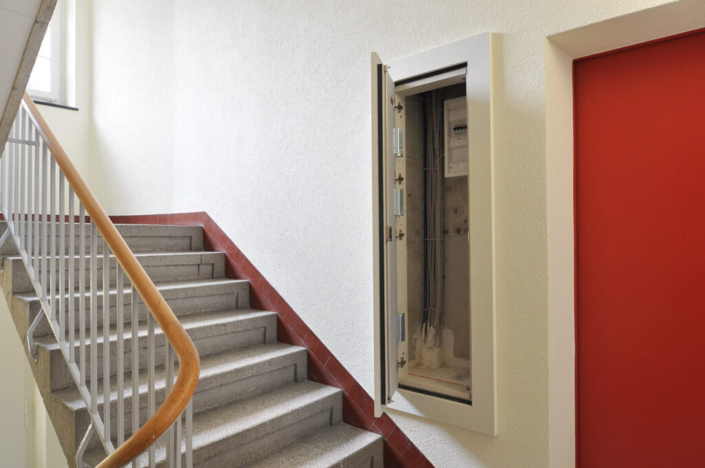Geöffnete Elektrofront neben einer Treppe mit Holzhandlauf