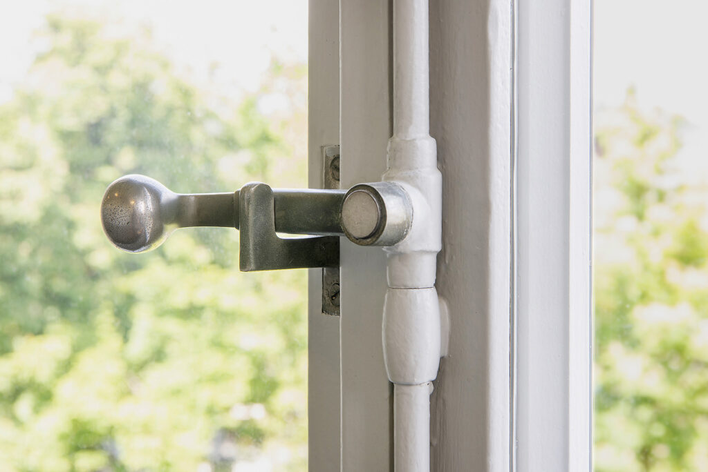 Detail eines weiss gestrichenen historischen Holzfensters mit metallischem Fenstergriff und Beschlag